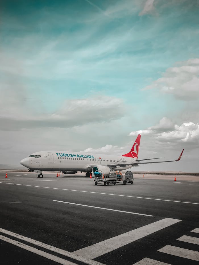Turkish Airlines plane parked on airport tarmac with clear blue sky and clouds.